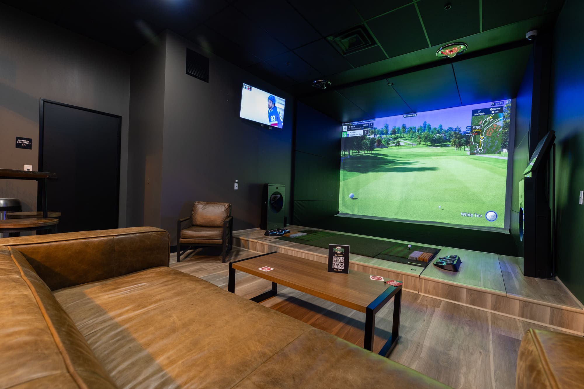 The Luxury Suite: leather seating and a low table facing the simulator screen, with a second screen on the wall.