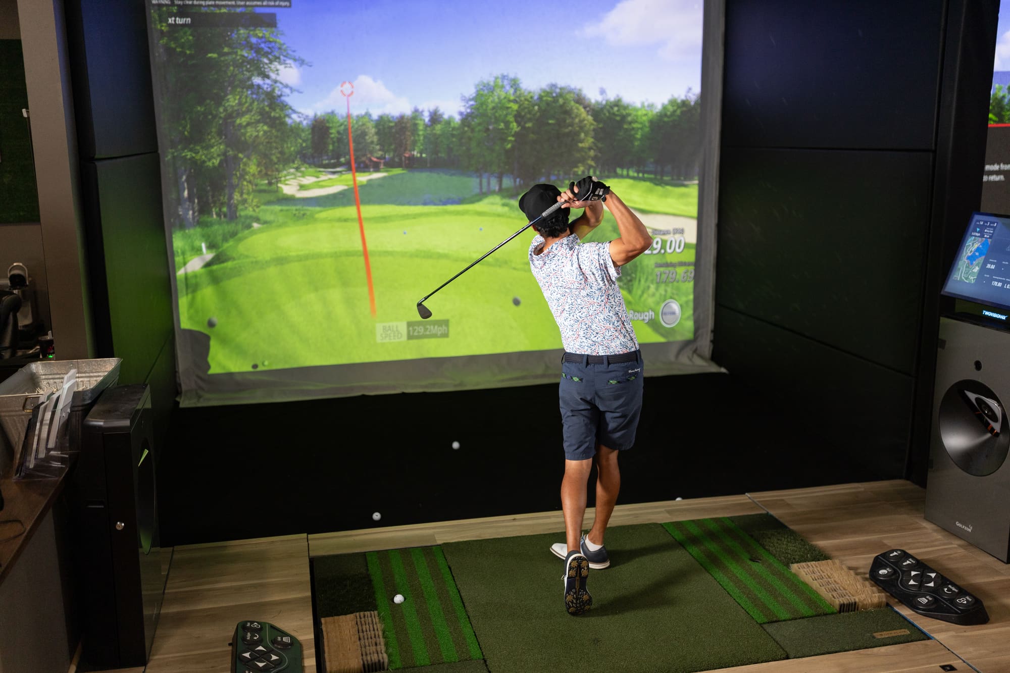 A golfer at the top of the follow-through in a Premium Bay, the shot tracking up the fairway on the simulator screen.